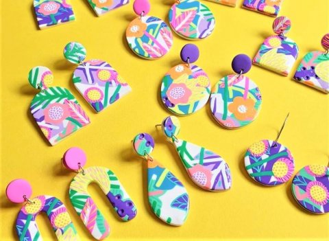 brightly colored polymer clay earrings in a variety of shapes with a floral-tropical design on a bright yellow background