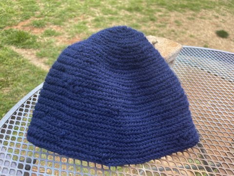 Blue hat that has been created with nalbinding sitting on a white outdoor table.