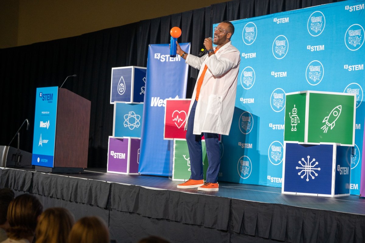 Man in white lab coat standing on a stage.