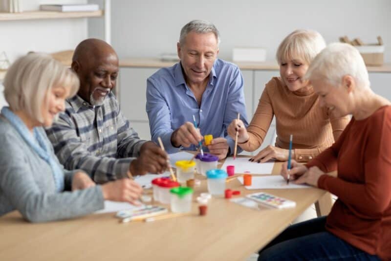 five adults sitting around a table painting together