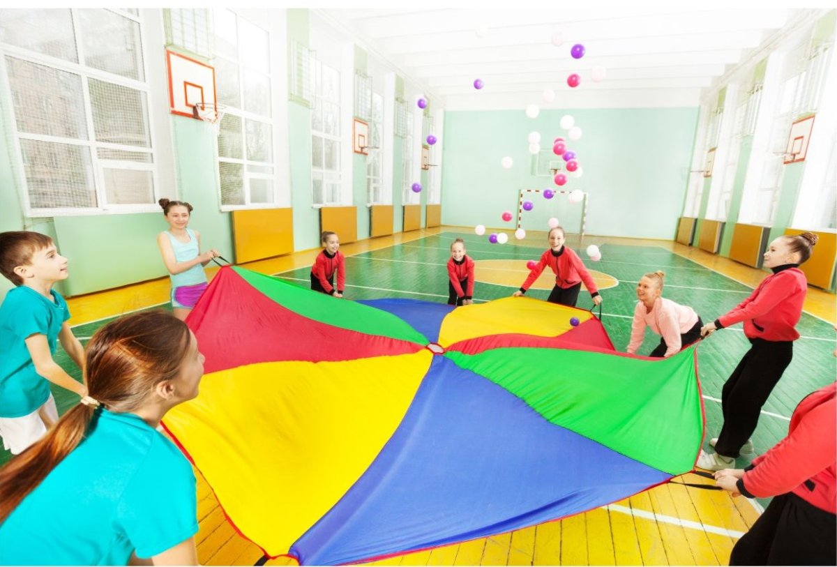 group of children around a colorful parachute in a gym