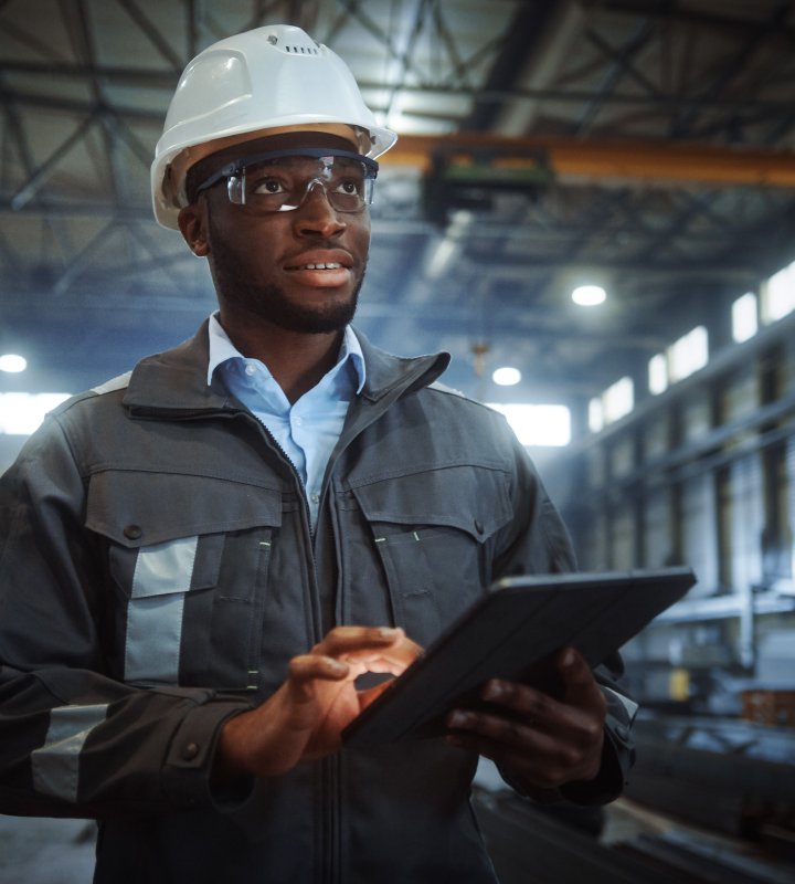 Industry Worker Wearing Safety Uniform and Hard Hat Uses Tablet Computer.