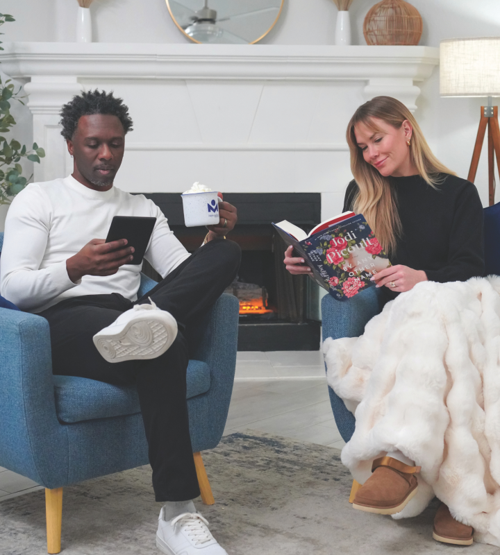 Diverse couple reading in front of a fireplace.